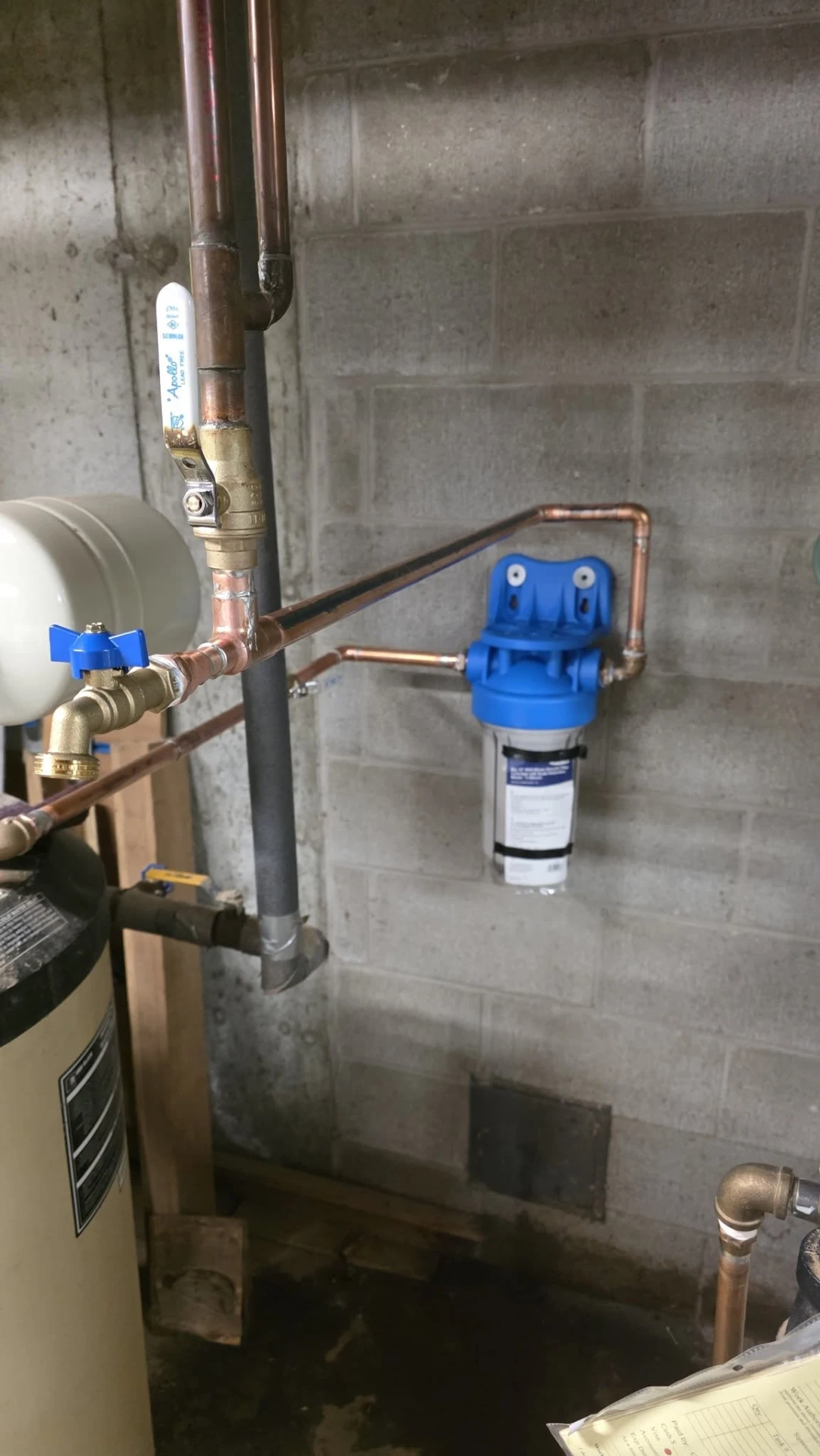 Whole-home water filter housing installed on copper supply lines beside a well tank